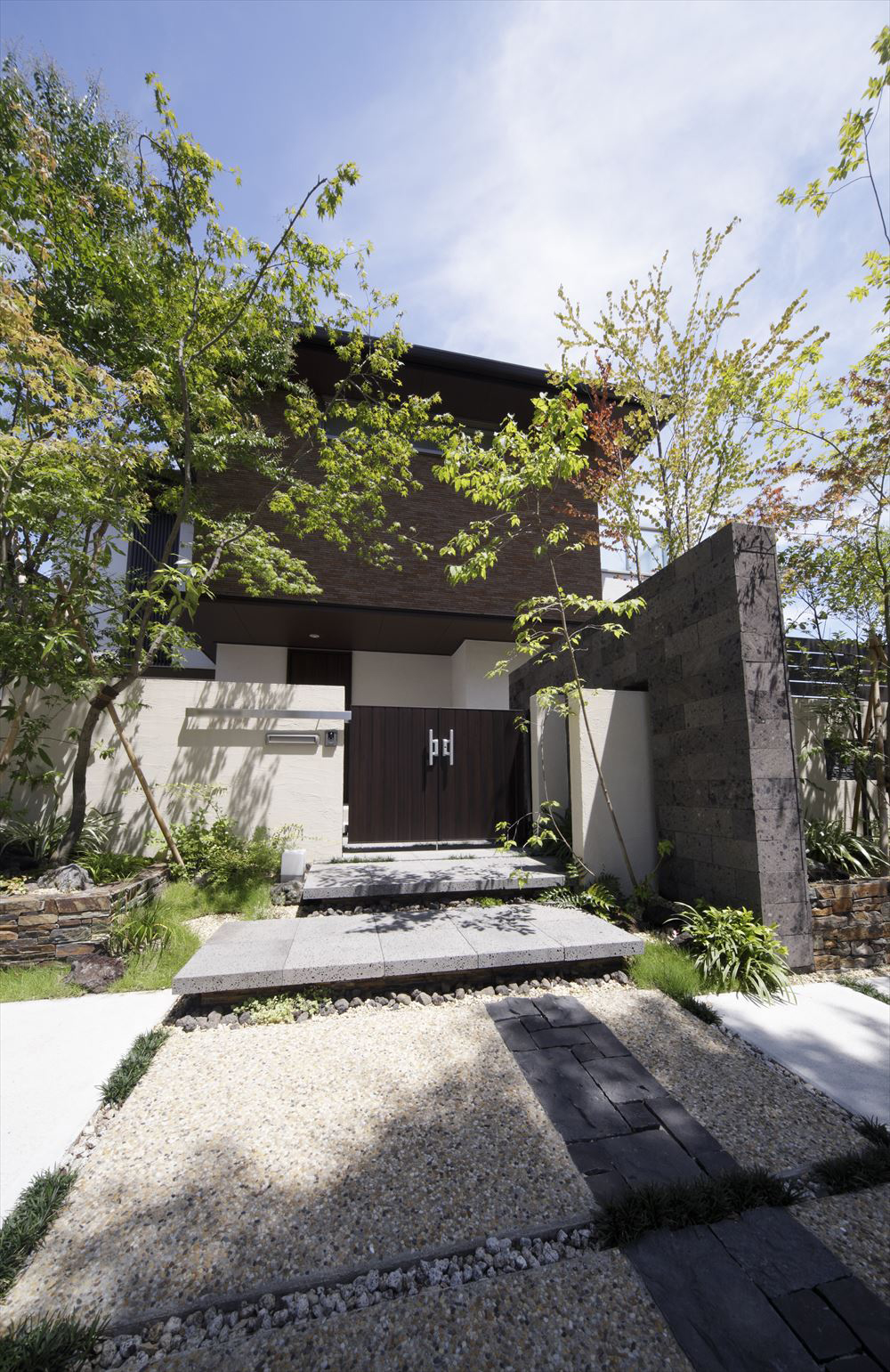 <p>住宅のモダンな外観と調和する玄関まわりの表情です。</p>
<p>石畳に落ちる木陰が心地よさを加えていますね。</p>